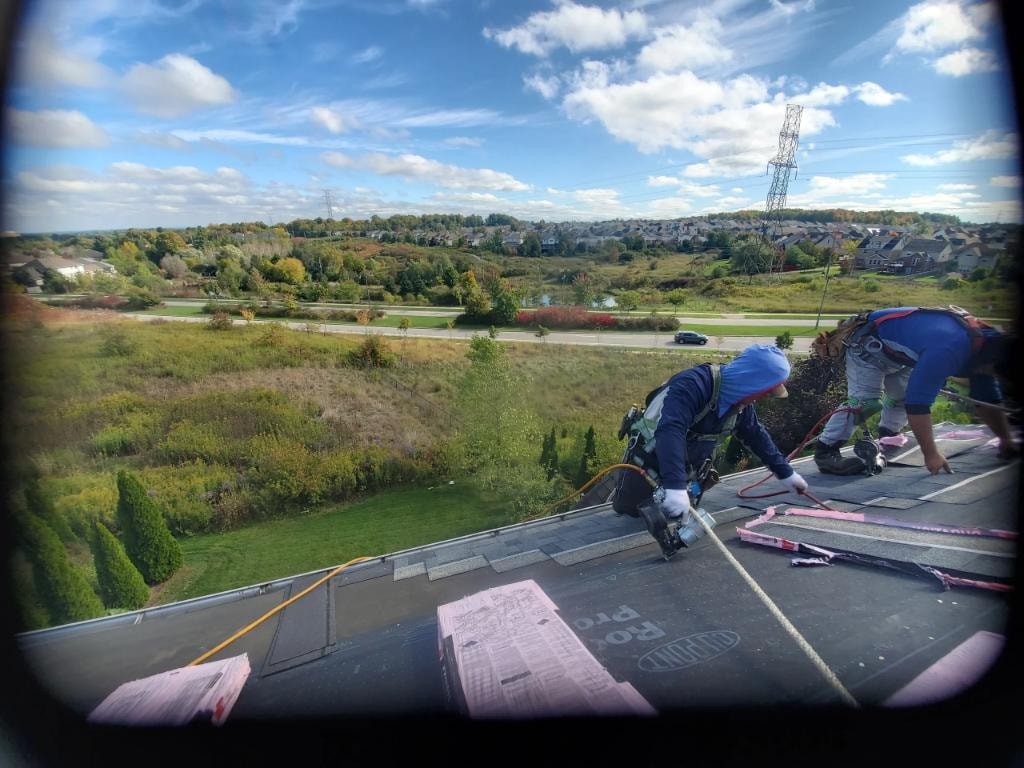 Roofers installing shingles with scenic suburban view